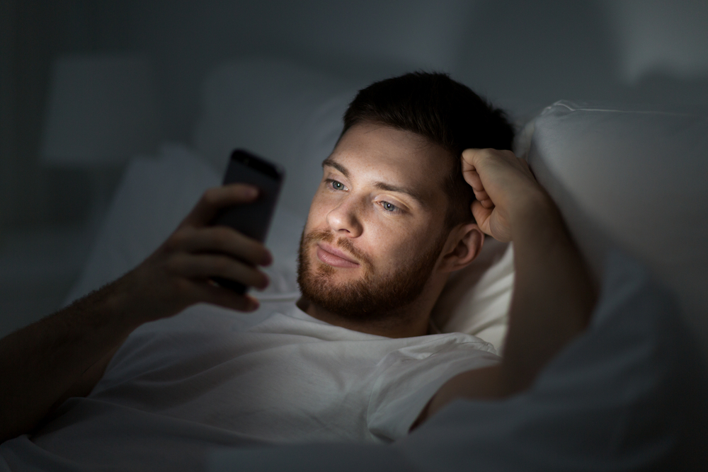 homme regarde son smartphone dans son lit