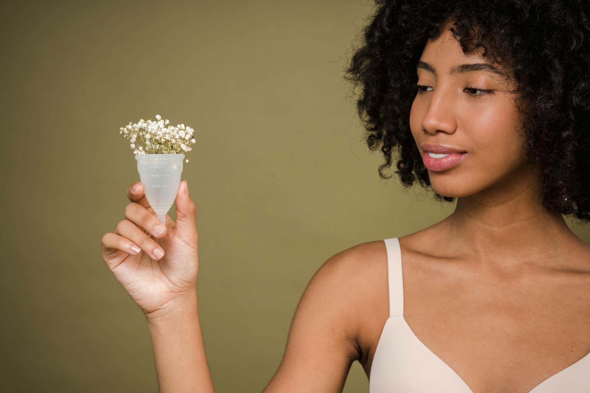 Une jeune femme métisse tient une coupe menstruelle avec des fleurs dans une main